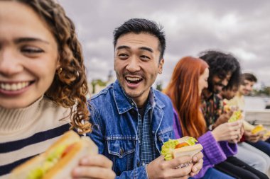 Bir adamla gülümseyen bir kadın, ikisi de şehirde taze sosisli yiyor..