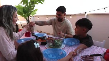 Gülümseyen bir aile terasta yemek yerken sohbet eder..