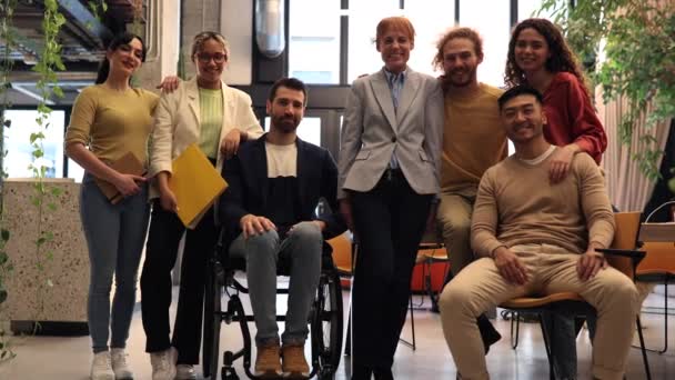 一个由六名专业人士组成的充满活力的团队 其中包括一名坐在轮椅上的专业人士 他们在办公室里微笑着 — 图库视频影像