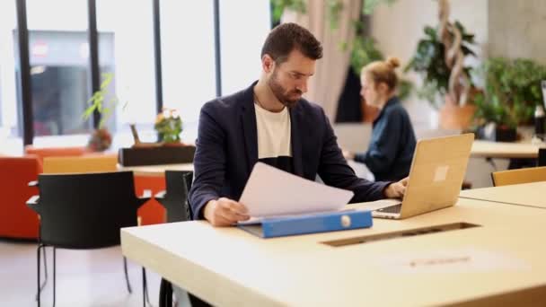 Человек Сосредоточенный Бумажной Работе Ноутбуком Освещенном Солнцем Офисе — стоковое видео