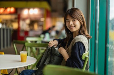 Kaldırımdaki kafede sırt çantalarını açan gülümseyen genç kadın..