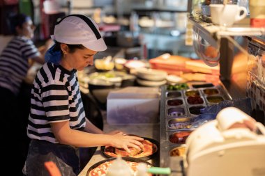 Becerikli şef, yoğun bir restoranın mutfağında pizzaya özenle malzeme ekliyor..