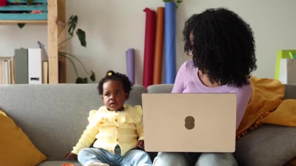 幼い母親は 赤ちゃんの横のラップトップで作業しながら微笑む — ストック動画