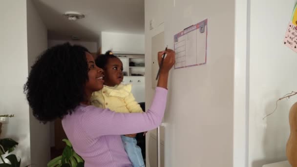 Anne Buzdolabına Bağlı Bir Planlamacıya Yazarken Bebeğini Tutuyor — Stok video