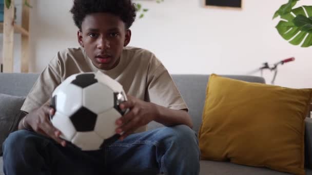 Улыбающийся Подросток Держит Футбольный Мяч Помещении Смотрит Футбол Телевизору Празднует — стоковое видео