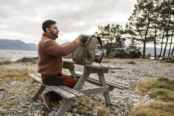 Hombre Suéter Acogedor Empaca Bolso Una Mesa Picnic Con Lago Imagen de stock