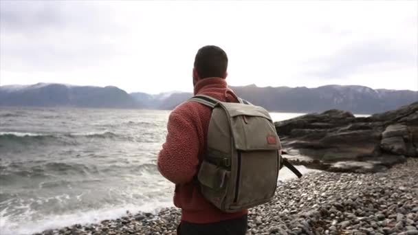 暖かいフリースのジャケットに覆われた旅行者は 海の侵入の瞬間 頑丈なフィヨルドの広大さを眺めています — ストック動画