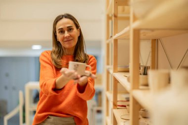 Bir çömlekçi yeni yapılmış seramik bardağı memnuniyetle sergiler..