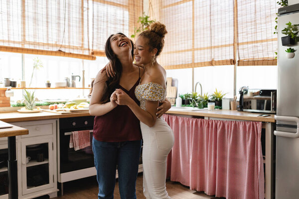 Joyful laughter fills the kitchen as two friends share a close and amusing moment in a homely atmosphere.