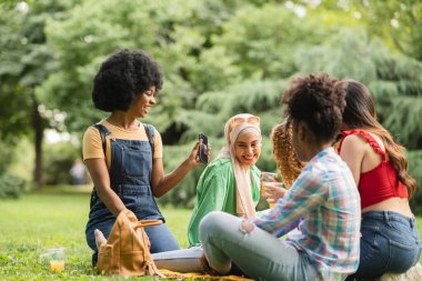 Yepyeni bir park ortamında, bir kadın akıllı telefonunu kullanarak arkadaşlarının pikniğinin keyfini yakalıyor..