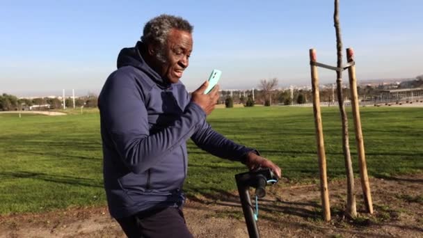 Gülümseyen Yaşlı Bir Adam Parktaki Motosikletiyle Güneşli Bir Günün Tadını — Stok video