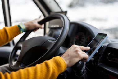 Karlı bir yolda yön bulmak için GPS tableti kullanan parlak sarı kazaklı bir sürücünün elleri..