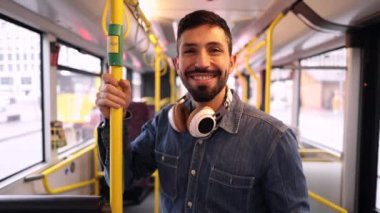Kulaklıklı neşeli bir adam parlak bir günde pencereden dışarı bakarken gülümsüyor, şehir otobüsünün keyfini çıkarıyor..
