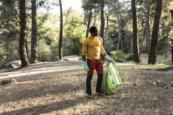 stock image A male hiker, equipped with gloves, carries a bag of collected litter, doing his part to maintain the natural beauty of the forest.