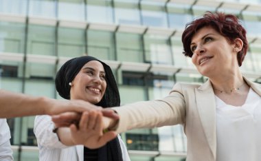 Farklı kültürlerden gelen iki gülümseyen kadın profesyonel modern bir ofis dışında birlik ve takım çalışması jesti olarak el ele tutuşuyor..