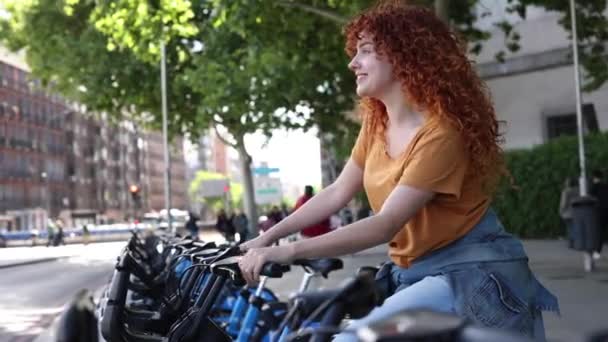 Kıvırcık Kızıl Saçlı Genç Kadın Bisiklet Paylaşım Programından Bisiklet Seçerken — Stok video