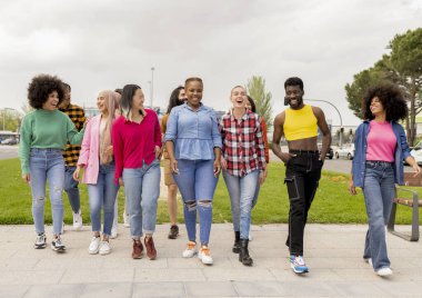 Bir grup farklı genç yetişkin parkta keyifli bir yürüyüş yapıyor, kahkaha ve dostluk gösterisi yapıyorlar..