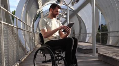 Tekerlekli sandalyedeki orta yaşlı bir adam tablet kullanmaya dalmış, modern bir şehir ortamında erişilebilirliği vurguluyor..
