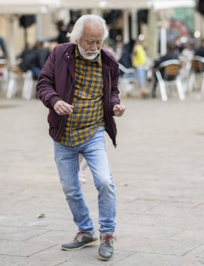 Yaşlı beyefendi hareketli bir şehir meydanında neşeyle dans ediyor. Özgürlüğü ve mutluluğu ifade eden heyecanlı adımları..