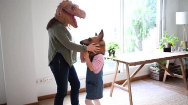 Bir anne ve çocuk, dinazor ve köpek maskeleri takarak birlikte eğlenceli bir an yaratarak yaratıcı bir oyun oynarlar. Evde Dinozor ve Köpek Maskeleri ile Eğlenceli Aile Eğlencesi