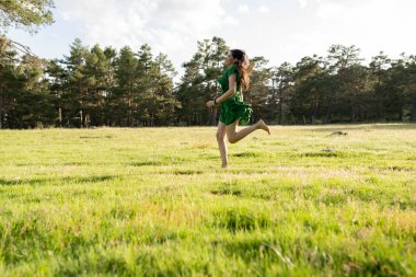 Canlı yeşil elbiseli genç bir kadın yemyeşil bir tarlada yalınayak koşuyor, saçları rüzgarda uçuşuyor, özgürlüğü ve neşeyi somutlaştırıyor..