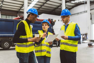 Güvenlik donanımlı çeşitli mühendisler planlarını tartışıyor ve bir endüstriyel tesiste belgeler tutuyorlar..