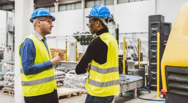 Sert başlık takan iki mühendis ve yüksek görünürlüklü yelekler endüstriyel bir tesiste bir tartışma içindeler..
