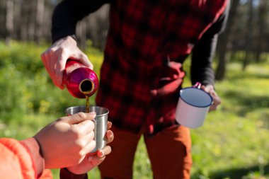 Genç bir adamın, termostan sıcak bir içeceği ormandaki metal bardaklara dökerek dışarıda geçirdiği anın tadını çıkardığı yakın plan..