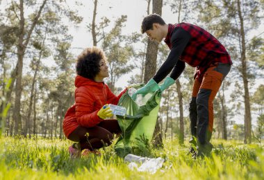 Orman parkında plastik atık toplayan iki yetişkin çevre koruma ve takım çalışmasını destekliyor..