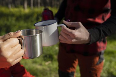 Ormanda metal ve emaye bardaklarını tokuşturup açık hava içkilerinin keyfini çıkaran iki insanın yakın çekimi..