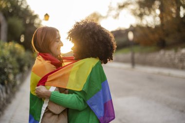 Gökkuşağı bayrağına sarılmış, açık havada günbatımının tadını çıkaran iki arkadaş.