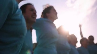 Mavi formalı kadın ragbi takımı güneşin altında bir kupa ile kollarını kaldırıp tezahürat yapıyor..