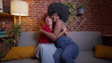 İki çok ırklı genç kadın, lezbiyen, eşcinsel çift, kanepede sımsıkı sarılıyorlar..