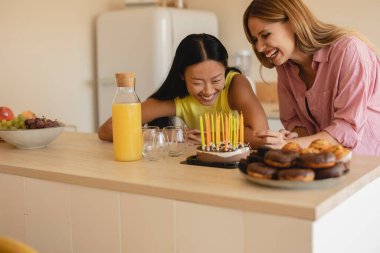İki genç kadın, doğum günlerini pasta ve mumlarla kutlarken birlikte gülüyorlar..