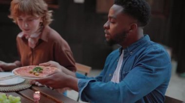 Çok ırklı arkadaşlar kırsal bir evde birlikte yemek yiyip pizza yiyorlar..