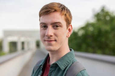 Sırt çantalı genç bir adamın portresi. Gülümsüyor ve patikada dikiliyor..