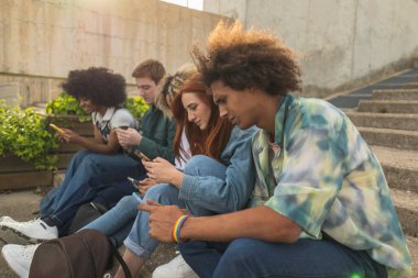 Basamaklarda oturan ve açık havada akıllı telefonlarına odaklanmış beş farklı yetişkinden oluşan bir grup..