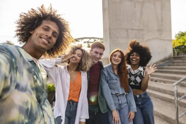 stock image Group of five diverse young adults smiling and posing for a selfie outdoors, capturing a joyful moment.