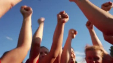 Bir grup kadın rugby oyuncusu kutlama ve birlik içinde yumruklarını kaldırarak takım ruhu ve kararlılığını gösteriyor..