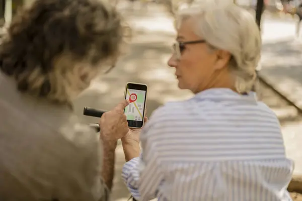 stock image Elderly couple using a smartphone GPS to navigate while outdoors on a sunny day.