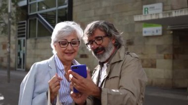 Dışarıda mutlu bir an yaşarken birlikte akıllı telefona bakan yaşlı bir çift..