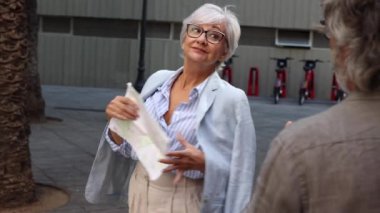 Elinde harita olan yaşlı bir kadın, partneriyle şehri gezerken fotoğraf çektirmek için poz veriyor..