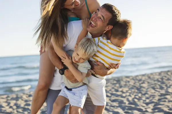 stock image Parents hugging their two young sons on a sunny beach, all smiling and enjoying the moment.