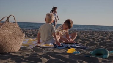 Aile sahilde eğleniyor, ebeveynler oynuyor ve çocuklar kumda koşuyor..