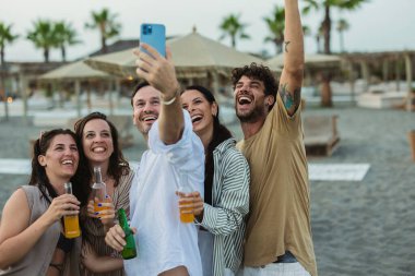 Bir grup arkadaş gülerek ve içkilerle selfie çekerken sahilde keyifli bir gün geçiriyorlar..