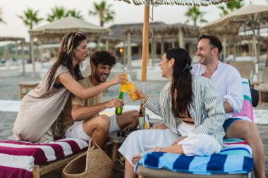 Bir grup arkadaş sazdan bir plaj şemsiyesinin altında rahatlarken içki içip kadeh kaldırıyorlar..