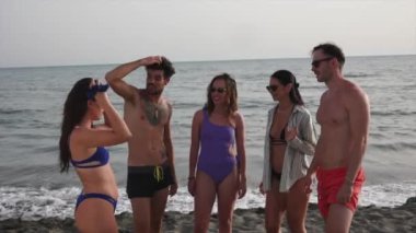 Bir grup yetişkin plaj gününün tadını çıkarıyor, kıyı şeridinde sohbet ediyorlar..