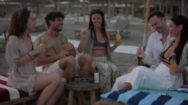 Bir grup genç yetişkin sahilde birlikte gülüp eğleniyor..