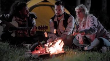30 'lu yaşlarında üç arkadaş marşmelov pişiriyor, kamp ateşinde gitar çalıyor, dışarıda eğleniyorlar..