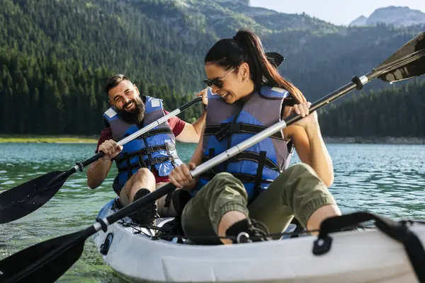 stock image A joyful couple in their 30s kayaking on a clear mountain lake, wearing life jackets and enjoying their adventure.